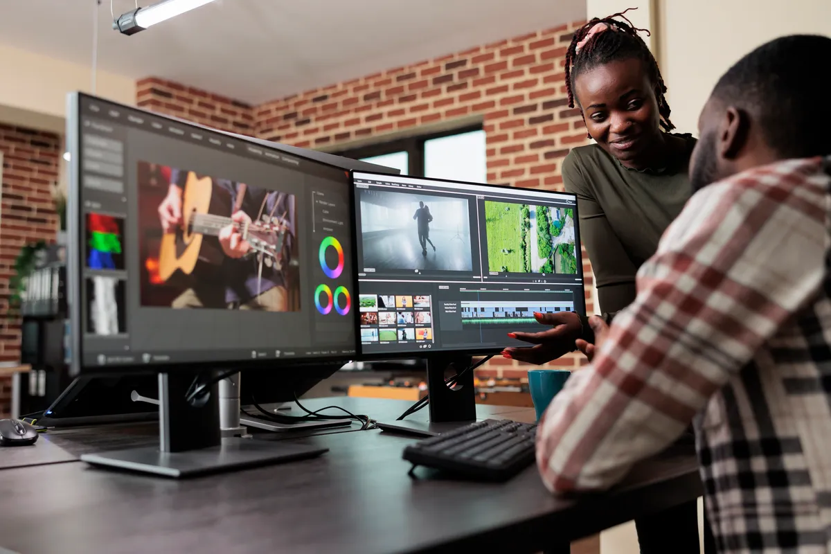Two people reviewing an edit together at a multi-screen workstation