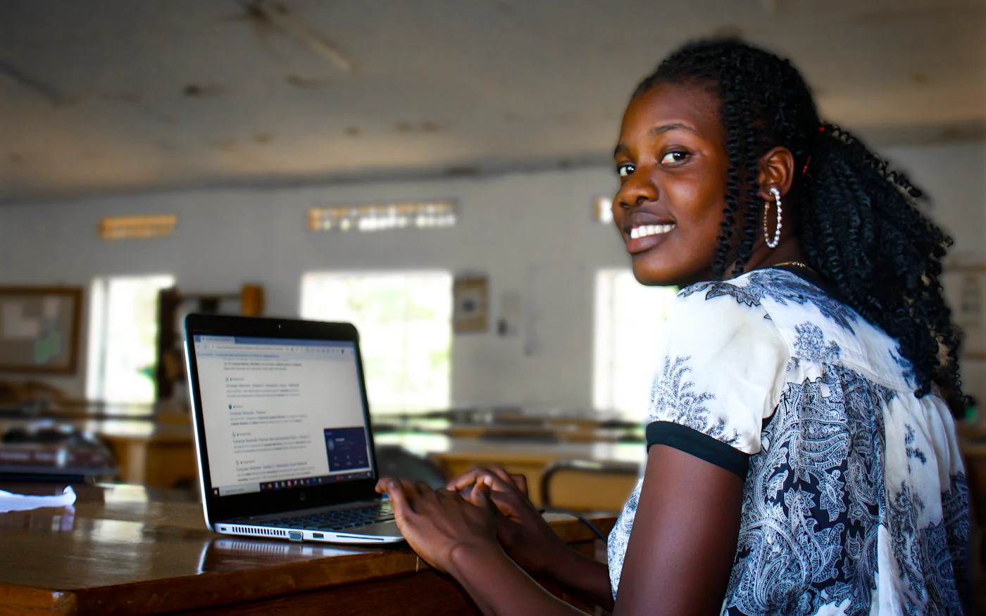 A student smiling while researching on a laptop in a classroom