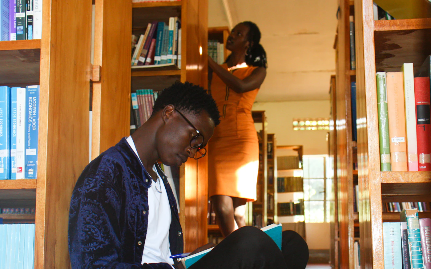 A student sitting between library shelves, reading and taking notes
