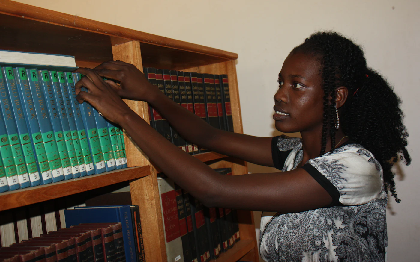 A student reaching for a reference volume on a library shelf