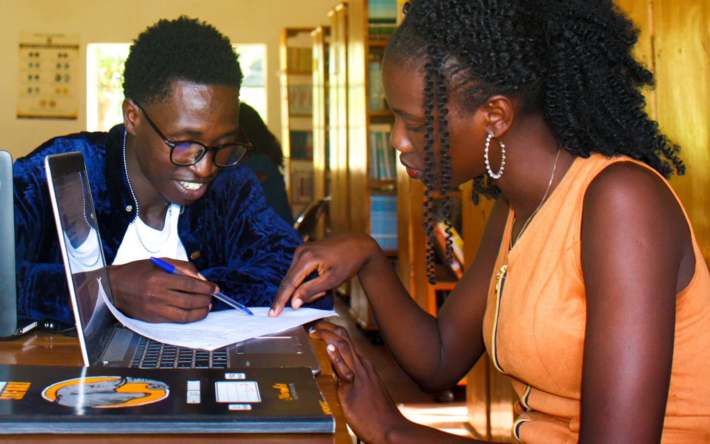 Two students working through an assignment together with a laptop in a school library